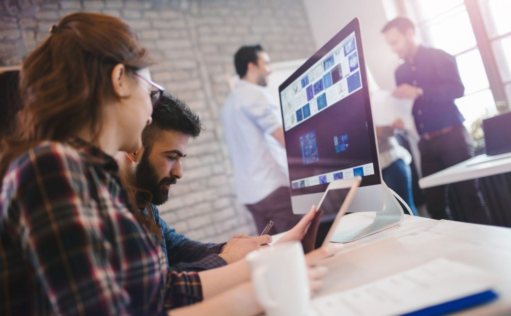 Une femme et un homme regardent une tablette, un cellulaire et un écran d'ordinateur.