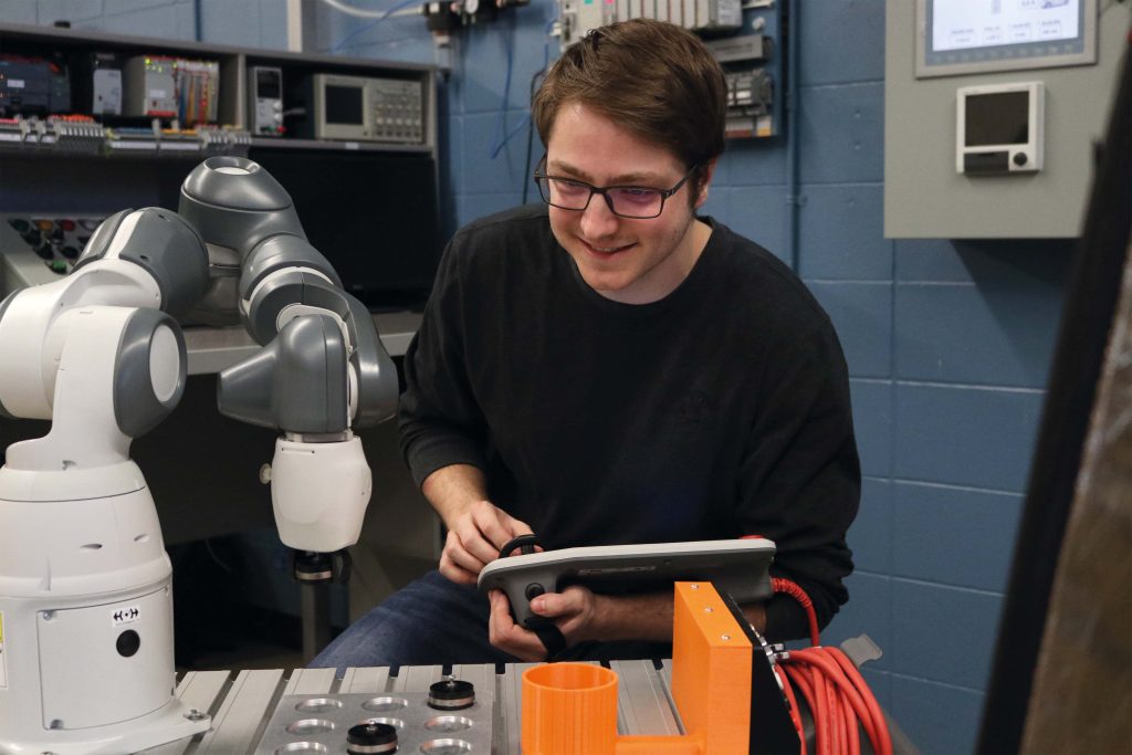 Étudiant dans un laboratoire manipulant la manette d'un bras robotisé.