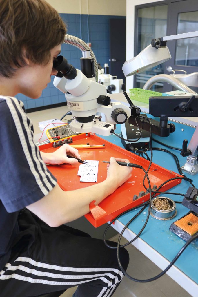 Étudiant regardant dans un appareil grossissant et manipulant des outils de soudure.