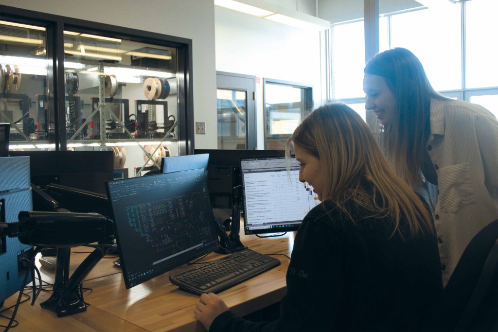 Deux étudiantes regardant des plans et un fichier de données sur un écran d'ordinateur.