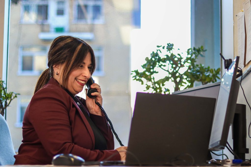 Femme au téléphone et regardant son ordinateur, le sourire aux lèvres.