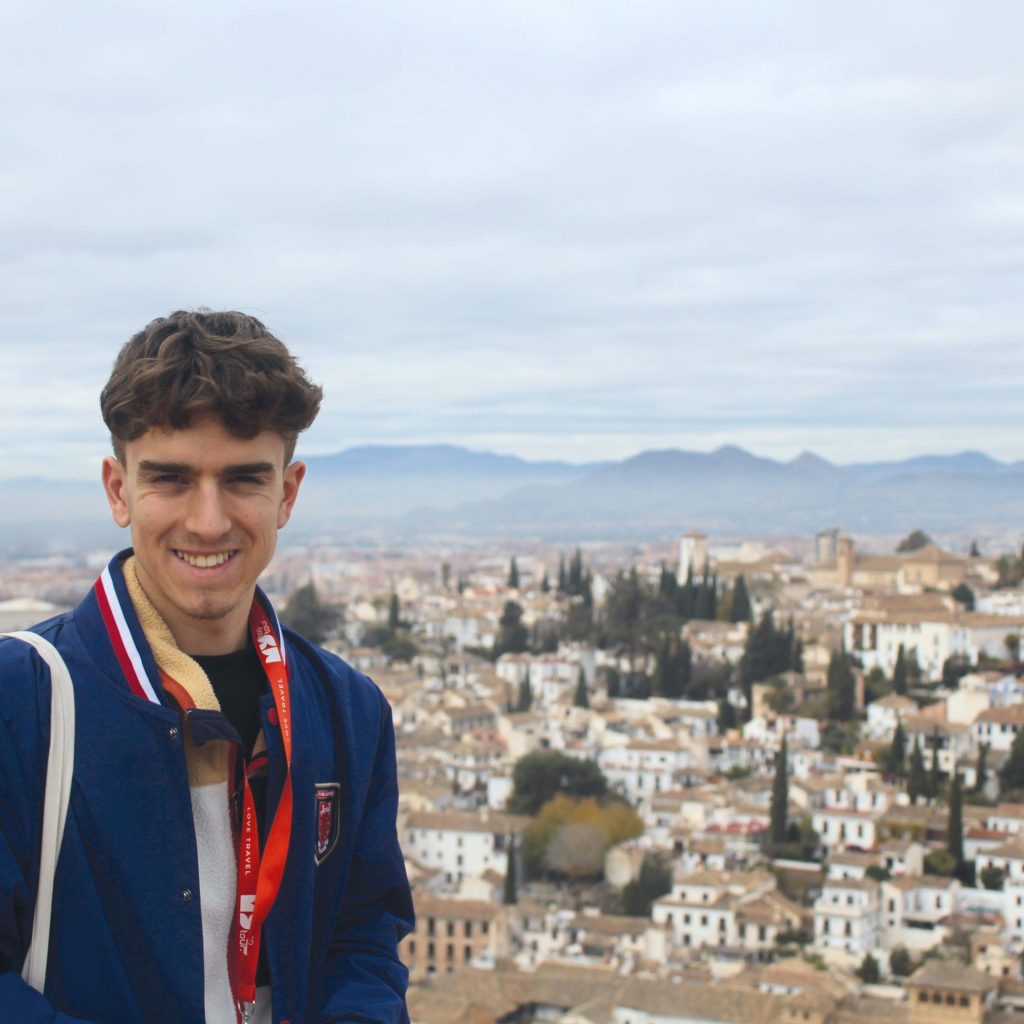 Étudiant qui sourit à la caméra devant un paysage de l'Espagne.