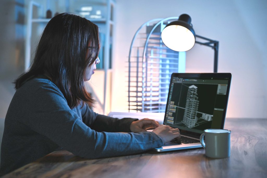 Femme assis à l'ordinateur, devant un logiciel avec un plan architectural d'un bâtiment.