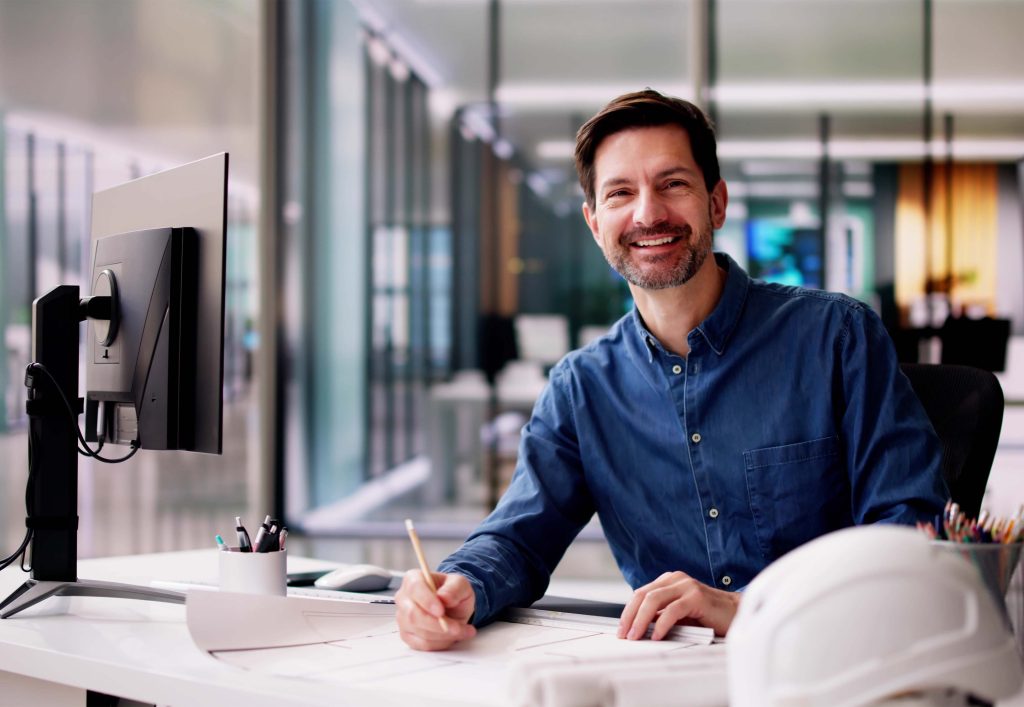Homme assis à un bureau avec avec des plans architecturaux.