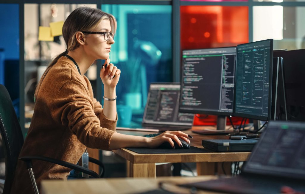 Femme travaillant devant des écrans d'ordinateur affichant du codage.