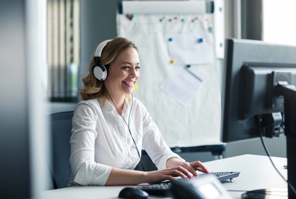 Femme écrivant à l'ordinateur, portant un casque d'écoute.
