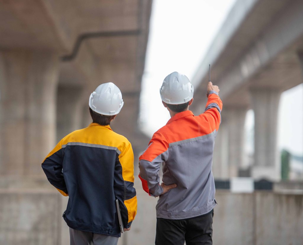 Deux hommes avec un casque de construction qui ont une conversation en regardant des ponts.