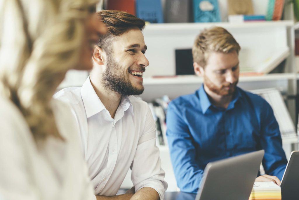 Trois personnes assis à un bureau pour une rencontre, prenant des notes sur des ordinateurs.