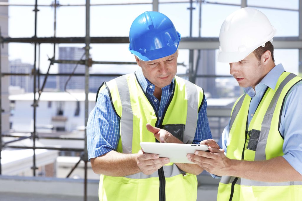 Deux hommes en uniforme de construction regardant une tablette électronique sur un chantier de construction.