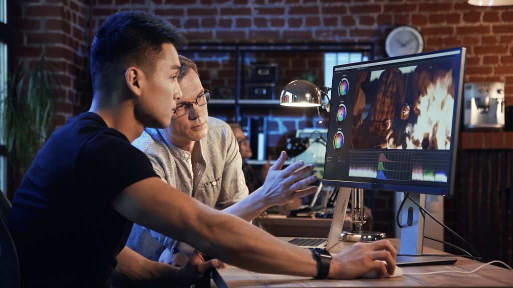 Deux hommes dans un bureau devant un écran d'ordinateur, qui regardent un logiciel de montage.