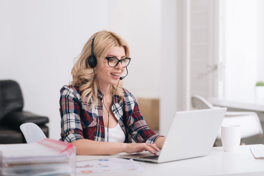 Femme assis dans un bureau devant son ordinateur portable, avec un casque d'écoute et un micro sur la tête.