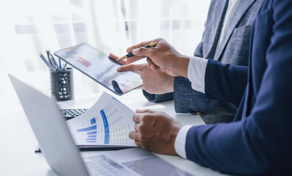 Deux hommes assis devant un bureau regardant des données imprimées et sur une tablette.