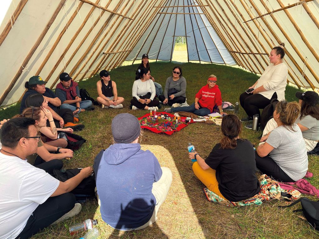 Personnes autochtones sous une tente, assis en cercle, assistant à un atelier.