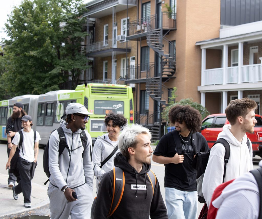 Étudiants internationaux se promenant dans le quartier Limoilou, un autobus derrière eux, le sourire aux lèvres.